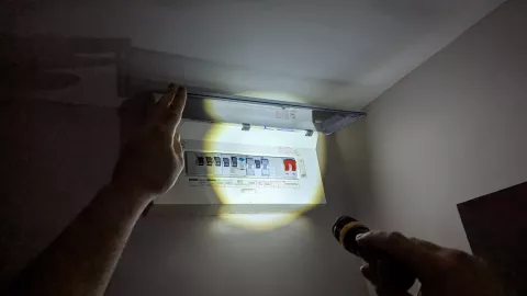 A person using a torch looking at the electrical panel during power loss
